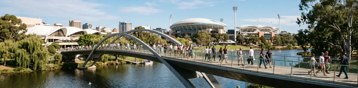 Adelaide Oval pedestrian footbridge crossing the River Torrens with the stadium visible beyond and people walking toward the ground