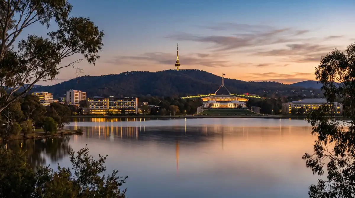 Canberra skyline at dusk with Black Mountain Tower visible and hotel buildings illuminated, reflections in Lake Burley Griffin
