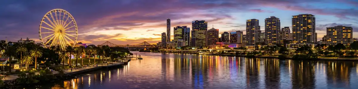 Brisbane South Bank skyline at dusk with hotel towers reflecting in the Brisbane River and the Wheel of Brisbane lit up