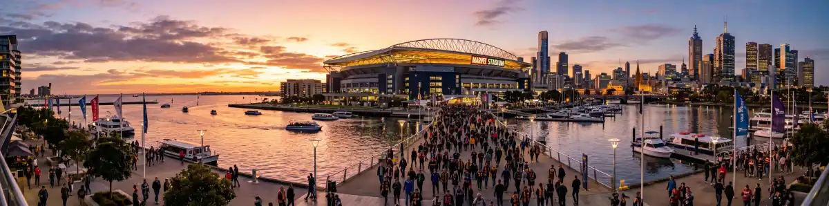 Marvel Stadium Docklands at sunset with the retractable roof glowing in golden light, Melbourne waterfront and harbour in the foreground