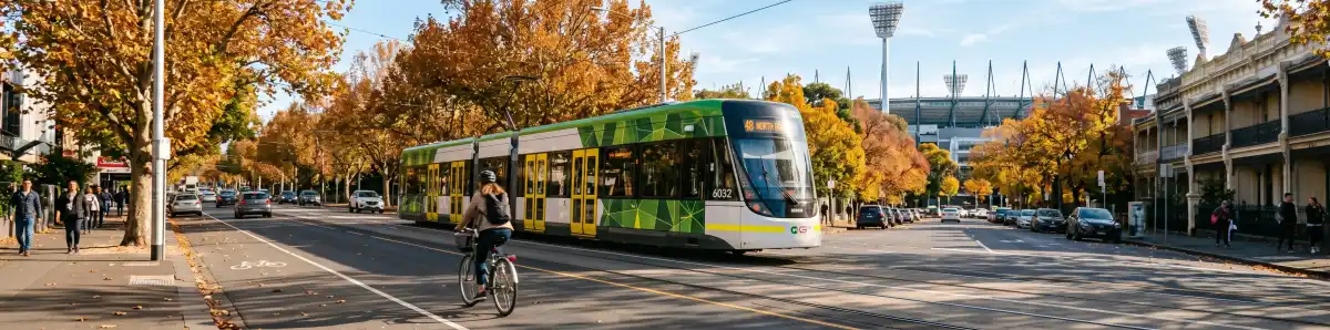 Melbourne tram on Wellington Parade with MCG light towers visible through autumn trees