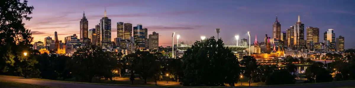 Melbourne CBD skyline at dusk with MCG light towers visible and hotel buildings illuminated